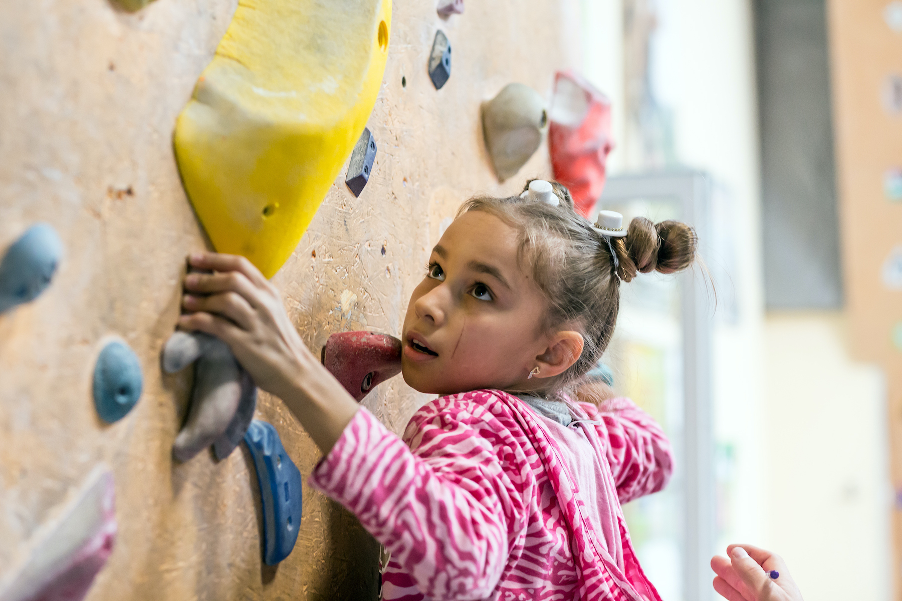 Junior Climber Girl shirt hanging on holds on climbing wall of indoor gym